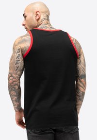 Top negru fără mâneci, cu margini roșii la decolteu și la orificiile pentru brațe, din bumbac, având o culoare uniformă fără modele sau grafice.