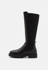 Botas negras hasta la rodilla con punta de cuero suave y suela de goma. Presentan paneles de tela elástica y una lengüeta en la parte superior para ponérselas fácilmente.