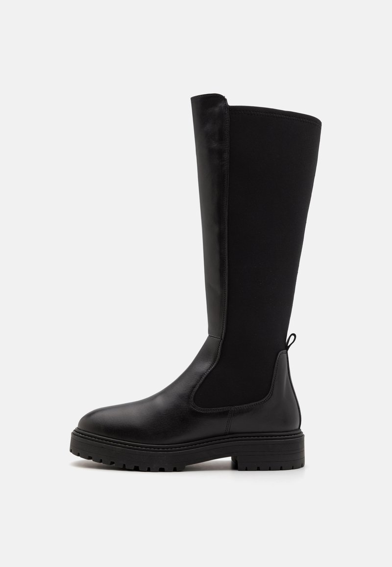 Botas negras hasta la rodilla con punta de cuero suave y suela de goma. Presentan paneles de tela elástica y una lengüeta en la parte superior para ponérselas fácilmente.