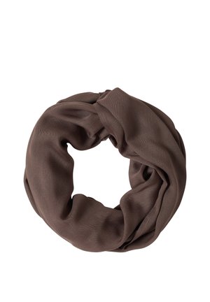 Femme souriante aux cheveux bruns portant un t-shirt blanc à manches courtes, une écharpe infinity marron et un jean bleu sur un fond clair.