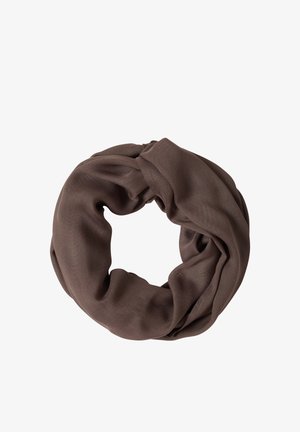 Smilende kvinde med brunt hår bærer en hvid kortærmet skjorte, brun infinity-sjal og blå jeans mod en lys baggrund.