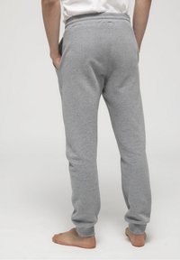Grå bomullsbyxor med avslappnad passform, elastiskt midjeband, sidofickor och ribbade muddarmar, sedd bakifrån med bara fötter.