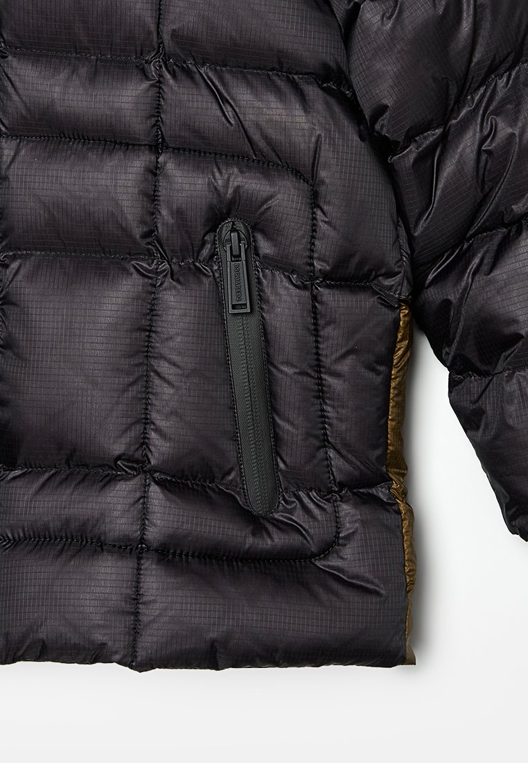 Sezione di giacca a vento nera trapuntata con tasca verticale con zip e manica imbottita visibile su sfondo bianco.