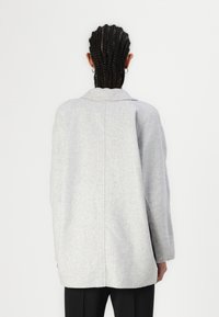 Abrigo de lana gris con un corte relajado, solapas anchas y mangas largas. Presenta una costura trasera recta y una textura suave.