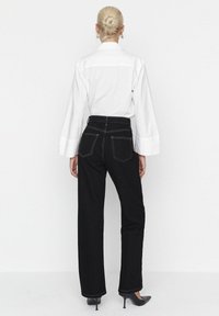 Černé džíny s vysokým pasem a rovným střihem, s kontrastním prošíváním, dvěma zadními kapsami a hladkou texturou. Kombinované s bílou košilí.