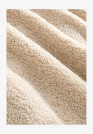 Tissu texturé de couleur crème avec une surface pelucheuse et douce. Le matériau semble doux et chaud, avec un motif ondulé.