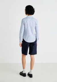 Lys blå stripete skjorte med lange ermer, kombinert med mørke denim-shorts. Svarte sko og grå sokker fullfører antrekket.