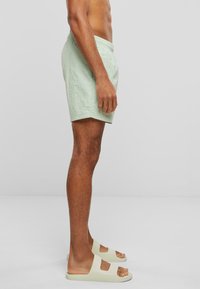 Lys grønn elastisk shorts med strikk i livet, over knærne, med en rynkete tekstur. Brukt sammen med kremfargede sandaler med to utskjæringer.