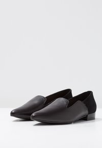 Svarta slip-on skor i slätt läder med spetsig tå och låg klack. Har mockadetaljer på sidorna och minimal sömnad.