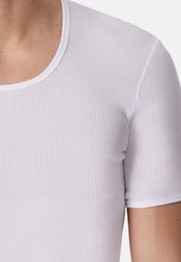 T-shirt blanc à rayures avec un col rond et des manches courtes, fabriqué en tissu léger avec une texture lisse.