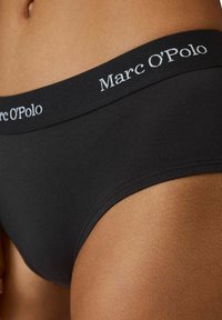 Slip di cotone neri con una texture liscia, dotati di un ampio elastico in vita etichettato "Marc O'Polo" in scritta bianca.