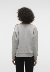 Felpa grigia oversize con scollo rotondo, spalle scese e tessuto testurizzato. Presenta dei fori decorativi sulle spalle e polsini a costine.