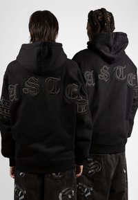 Las sudaderas negras cuentan con un gran texto bordado en la parte posterior. El tejido parece suave, con un ajuste relajado y puños y dobladillo acanalados.