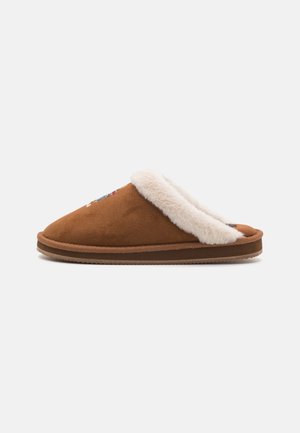 Chausson en daim marron à enfiler avec doublure en fausse fourrure blanche et semelle épaisse, présenté en profil latéral sur un fond uni.