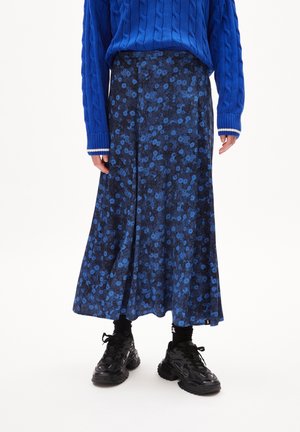 Person iført en blå kabelstrikket sweater, sort og blå blomsterprintet midinederdel, sorte sokker og sorte chunky sneakers på en hvid baggrund.
