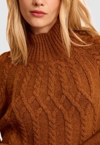 Maglione marrone a maglia con un alto colletto a costa. Presenta un motivo a trecce testurizzato su tutta la stoffa, creando un'aspetto accogliente.