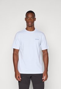 Camiseta de algodón blanca de manga corta y cuello redondo, con un pequeño logo azul de Patagonia en el lado izquierdo del pecho.