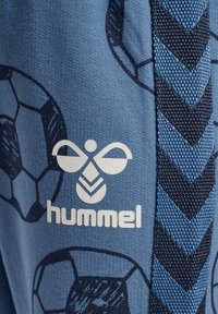 Blå byxor med ett mönster av fotbollar och en vit "hummel"-logotyp. Sidopanel med ett texturerat, mörkblått chevronmönster.