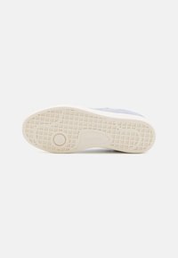Zapatilla Lacoste con un upper de ante azul claro y una suela de goma texturizada. La suela tiene un patrón en cuadrícula y es de color crema.