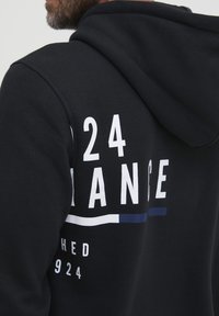 Felpa nera con cappuccio, caratterizzata da grafiche bianche, tra cui "24" e "CHANGE", con un accento orizzontale blu. Tessuto morbido e vestibilità standard.