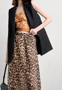 Svart ärmlös blazer i kombination med en orange mönstrad topp och en flödande leopardmönstrad kjol. Kjolen har en elastisk midja.