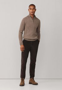 Bruine geribbelde gebreide trui met een ritskraag, gecombineerd met donkerbruine corduroy broek en lichtbruine veterschoenen. Eenvoudig, modern ontwerp.