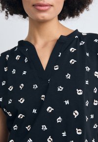 Schwarzes Oberteil mit V-Ausschnitt, aus weichem Stoff, verziert mit bunten Cartoon-Charakter-Drucken und weißen Akzenten im gesamten Design.