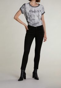 Černé skinny džíny v kombinaci s grafickým šedým a černým topem se textem a designem městské krajiny. Modelka má na sobě černé boty na podpatku.