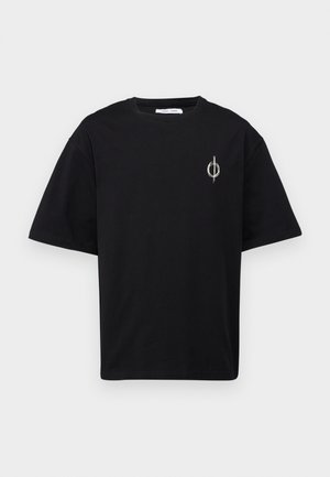 Camiseta negra de manga corta con un pequeño patrón de líneas circulares blancas y un logo de líneas verticales en el lado izquierdo superior del pecho sobre un fondo liso.