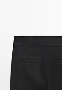 Pantalon noir présentant une texture de tissu lisse, deux poches arrière et une ceinture ajustée sans attaches visibles ni décorations.
