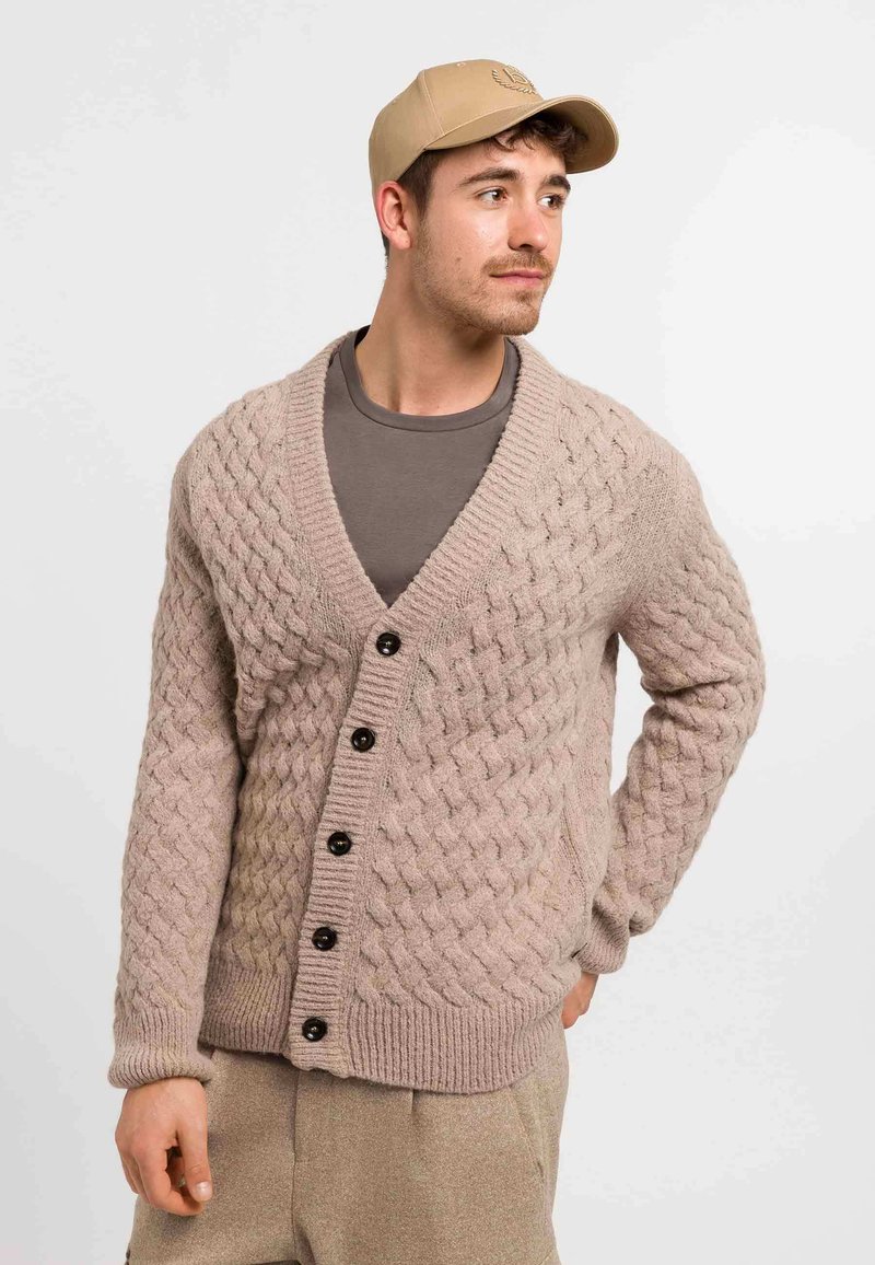 Beige gestrickte Strickjacke mit Kabelmuster, V-Ausschnitt, fünf schwarzen Knöpfen, gerippten Bündchen und einem lässigen Schnitt über einem grauen Hemd.