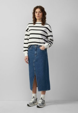 Pull à manches longues rayé noir et blanc, associé à une jupe en denim de longueur genou avec une fente sur le devant. Porté avec des baskets grises et noires.