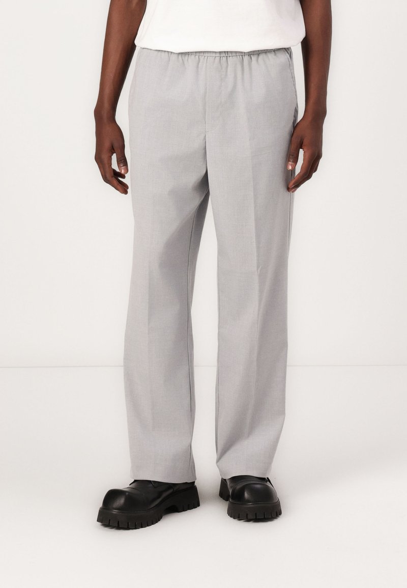 Hellgraue, elastische Hosen mit geradem Bein, aus einem glatten Stoff, kombiniert mit schwarzen klobigen Schuhen.