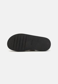 Black shoe sole with a textured surface, featuring horizontal grooves for grip. Smooth edges and rounded toe shape with subtle branding.