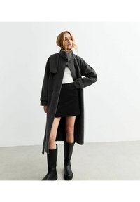 Grau Wolle mantel mit einem doppelt belegten Design, weitem Kragen und umgeschlagenen Ärmeln, kombiniert mit einem schwarzen Minirock und knielangen schwarzen Stiefeln.