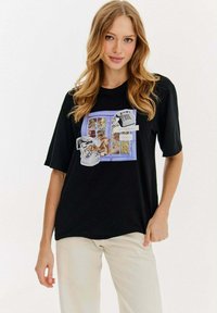 Czarna koszulka z krótkim rękawem z graficznym wzorem przedstawiającym okno, psa, czaszkę i tekst. Wykonana z miękkiego materiału o luźnym kroju.