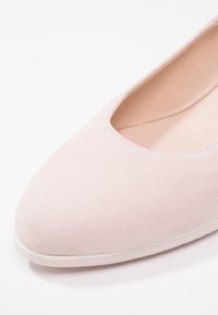 Ballerine en daim rose clair avec bout arrondi et semelle basse, montrée en gros plan sur fond blanc.