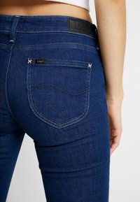 Jeans de mezclilla azul oscuro con una textura suave, una etiqueta de cuero en la cinturilla y costuras distintivas en los bolsillos traseros.