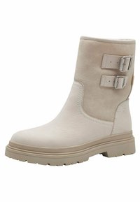 Bottine beige avec une finition en daim doux, deux boucles métalliques réglables, une semelle extérieure texturée et un design à bout rond.