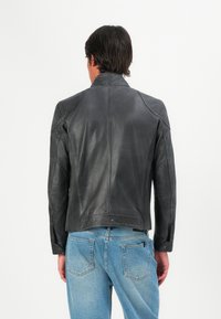 Chaqueta de cuero negra con un diseño estructurado, que presenta detalles acanalados en los lados y un alto cuello, combinada con jeans de mezclilla azul claro.