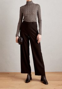 Svarta vida byxor i kombination med en åtsittande svart och gräddfärgad randig polotröja. Modellen håller en liten svart väska och har på sig svarta klackstövlar.