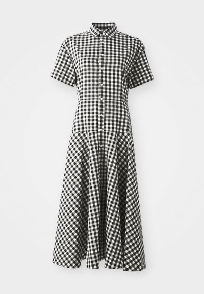 Knapplang kjole i svart og hvit rutete mønster. Korte ermer, strukturert liv, og en utrøstet skjørt som strekker seg under kneet.