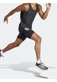 Débardeur de sport noir et shorts noirs avec des rayures blanches, présentant un design ajusté et des chaussures de course. Mouvement dynamique capturé.