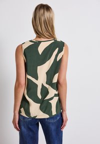 V bezramenném topu v zelené a béžové barvě s odvážným abstraktním vzorem. Vyrobeno z lehkého materiálu s uvolněným střihem a kulatým výstřihem.