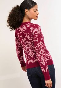 Pulover tricotat în bordeaux cu un model floral roz, mâneci lungi, manșete și tiv cu lână, asociat cu blugi din denim închis.