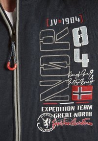 Navy Zip-Jacke mit gestickten Grafiken in Weiß, Rot und Beige, einem Patch mit der norwegischen Flagge und strukturiertem Strickstoff.