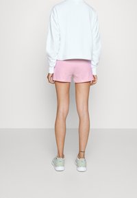 Pantalones cortos rosa claro con un corte relajado, combinados con un sudadero blanco corto y zapatillas verdes. Tejido suave y diseño sencillo.