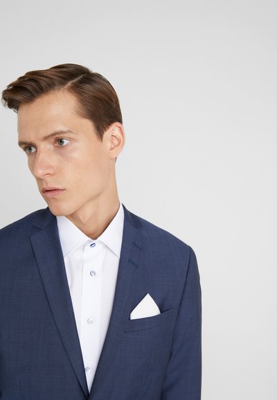 Navy blue suit jacket with a slim fit, textured fabric, notch lapels, and a white dress shirt featuring a pocket square and blue button accents.