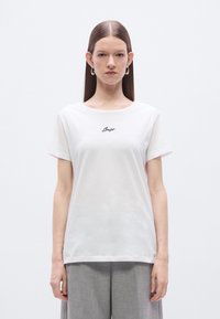 Λευκό βαμβακερό μπλουζάκι με στρογγυλή λαιμόκοψη και κοντά μανίκια. Διαθέτει μαύρο κεντημένο κείμενο "Bess" στο μπροστινό μέρος. Μαλακή υφή.