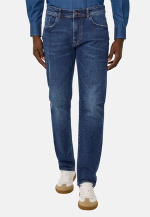 Jeans de mezclilla azul oscuro con corte recto, ligeras desgastaciones en los muslos y costuras en contraste. Combinados con zapatillas blancas y acentos claros.